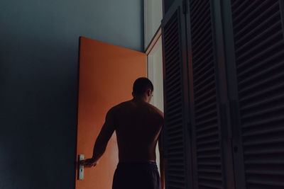 Rear view of shirtless man standing against wall at home