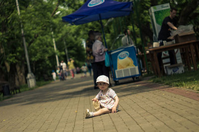 Portrait of girl sitting on footpath at park