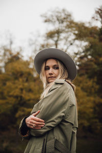 Portrait of young woman wearing hat standing against trees