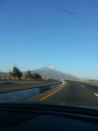 Road leading towards mountains against blue sky