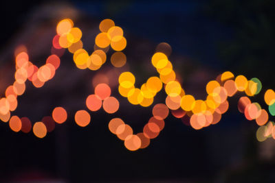 Defocused image of illuminated christmas lights against sky at night