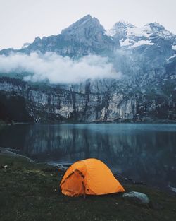 Tent on shore by oeschinen lake against rocky mountains at swiss alps