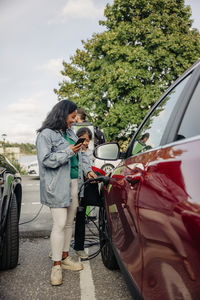 Smiling woman with daughter charging electric car at station