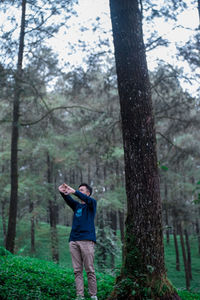 Man stretching hands while standing by trees in forest