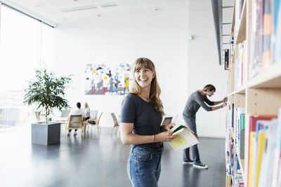 Happy young woman holding books in library