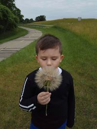 Boy holding dandelion while standing on grassy field
