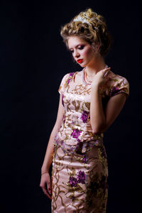 Thoughtful woman in evening gown standing against black background