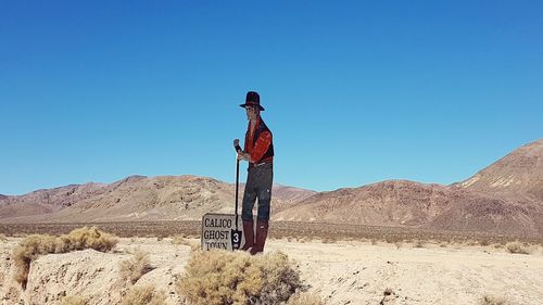 Man with umbrella on desert against clear blue sky