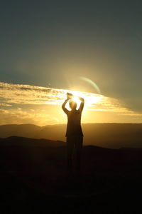 Silhouette woman standing on street against sky during sunset