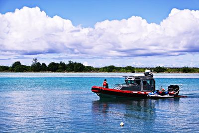 Boats in calm sea against cloudy sky