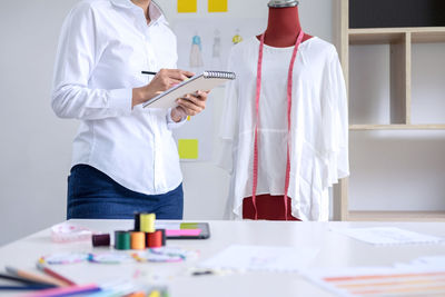 Midsection of female fashion designer drawing on book in office