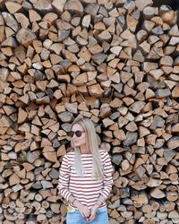 Woman wearing sunglasses standing against woodpile