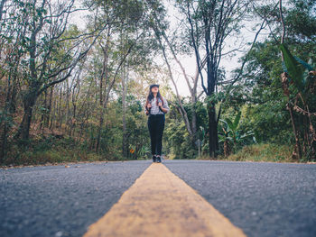 Woman standing on road amidst trees in forest