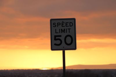 Close-up of road sign against orange sky