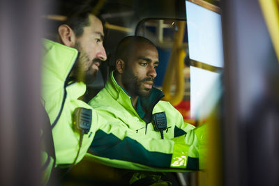 Male paramedics discussing while sitting in ambulance at parking lot