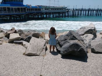 Rear view of girl standing by rocks by sea