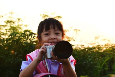 Close-up portrait of girl holding camera against sky