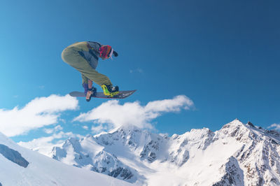 Low angle view of man standing on snowcapped mountain against clear blue sky