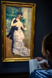 Cropped image of woman drawing in book while looking at painting