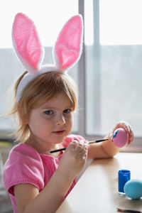 Little girl in easter bunny ears painting colored eggs. easter at home and craft concept.