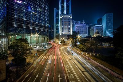 Light trails on illuminated city against sky at night