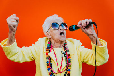 Senior woman wearing colorful jewelry and sunglasses singing against red background