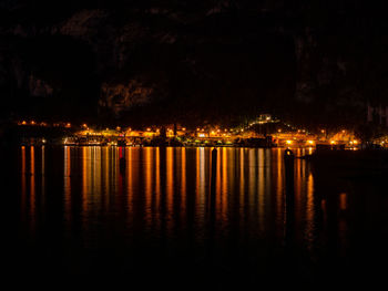 Illuminated buildings by lake against sky at night