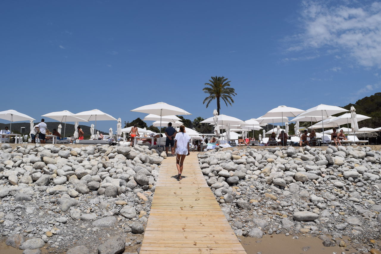 the way forward, clear sky, built structure, architecture, person, lifestyles, building exterior, men, blue, walking, leisure activity, sky, copy space, footpath, sunlight, pathway, beach, walkway, cobblestone