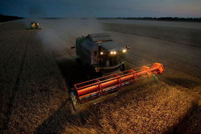 High angle view of combine harvesters working on wheat field at night