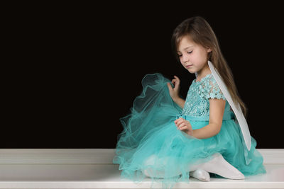 Little girl blonde sits on the windowsill in a green dress angel wings behind her shoulders