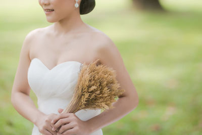 Midsection of bride holding bouquet while standing at field