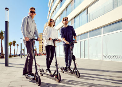 Friends using push scooters in city on sunny day