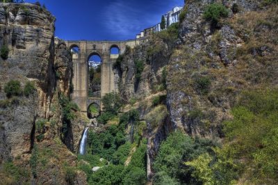 Low angle view of puente nuevo amidst rock formations against blue sky