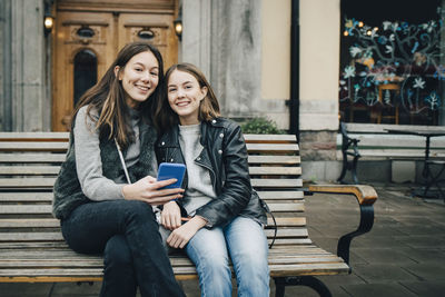 Smiling young woman using mobile phone while sitting on seat