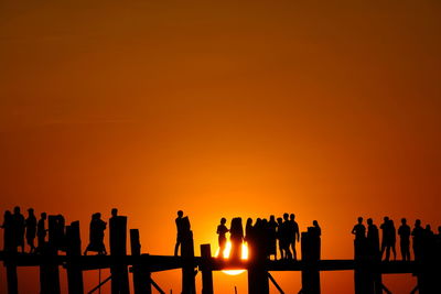 Silhouette people standing by railing against orange sky