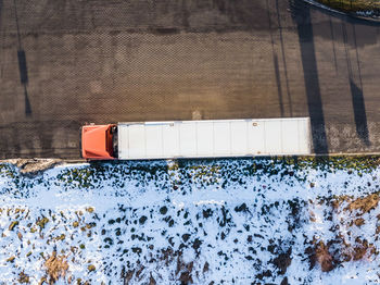 Aerial follow shot of white semi truck with cargo trailer attached through industrial warehouse