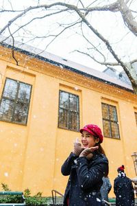 Portrait of smiling woman standing against building during snow fall