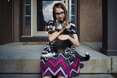 A pre teen girl holding her gray cat on the front porch