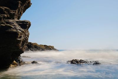 Rock formation in sea against clear sky