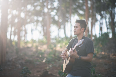 Young man using guitar while standing on land