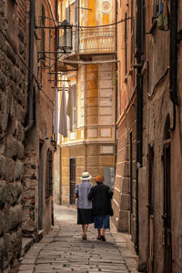 Rear view of people walking in alley amidst buildings in city