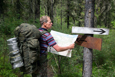 Side view of man with backpack reading map while standing in forest