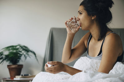 Woman taking medicine while sitting on bed at home