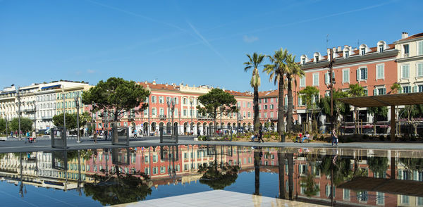 Buildings by river against clear blue sky