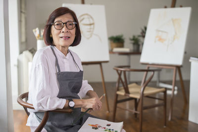 Portrait of woman sitting on chair against canvas at home