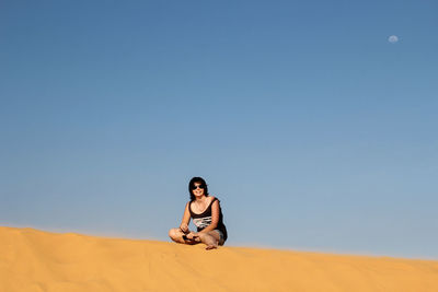 Happy woman resting on sand against clear blue sky
