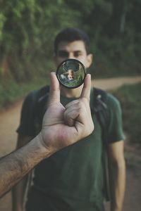 Cropped hand holding lens with reflection of man in forest