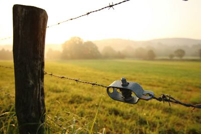 Close-up of barbed wire on wooden post at field against sky