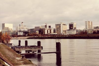 Buildings by river against sky in city