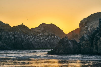 Rock formations in sea against sky during sunset